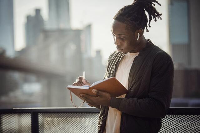 Young adult writing in a notebook with headphones in. Ad for Chinese language class.