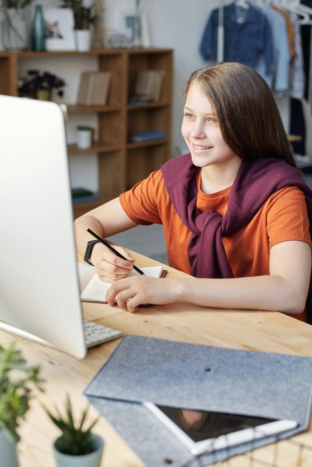 woman in orange shirt writing on white paper as she takes online course